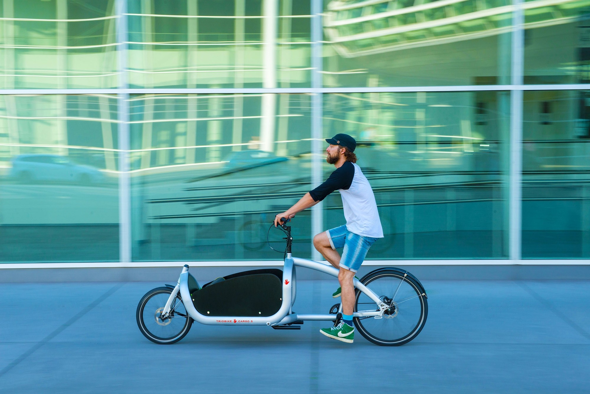 Ein Mitarbeiter fährt mit dem Triobike Cargo Lasten e-Bike durch die Stadt und transportiert Dinge.