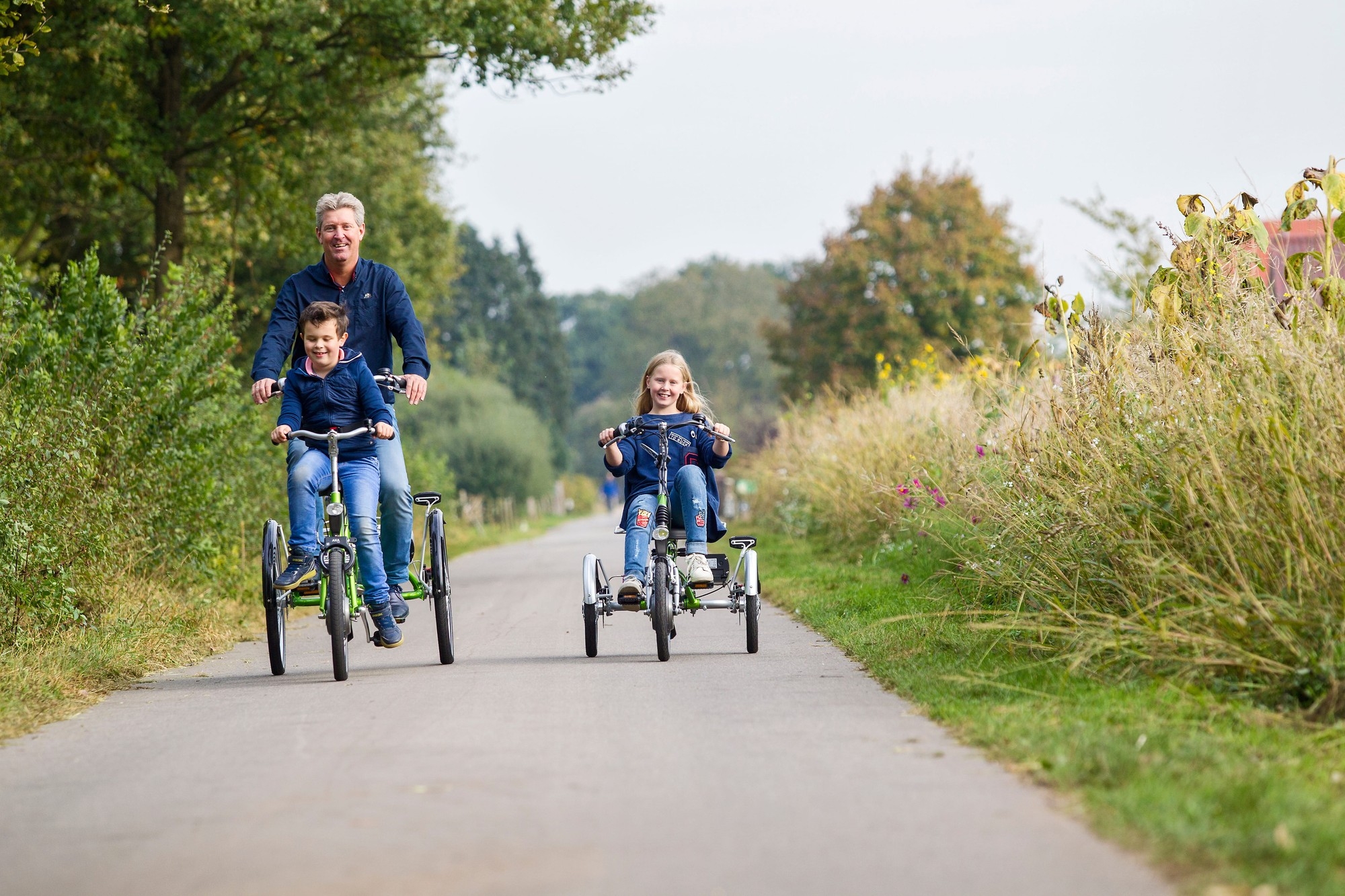 Das Bild zeigt zwei Van Raam Dreiräder, die auf einem breiten Radweg fahren.