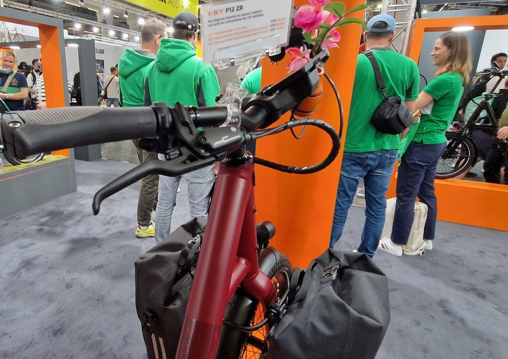Eine Detailbild einer Messe, im Vordergrund ein e-Bike, im Hintergrund stehen verschiedenen Personen