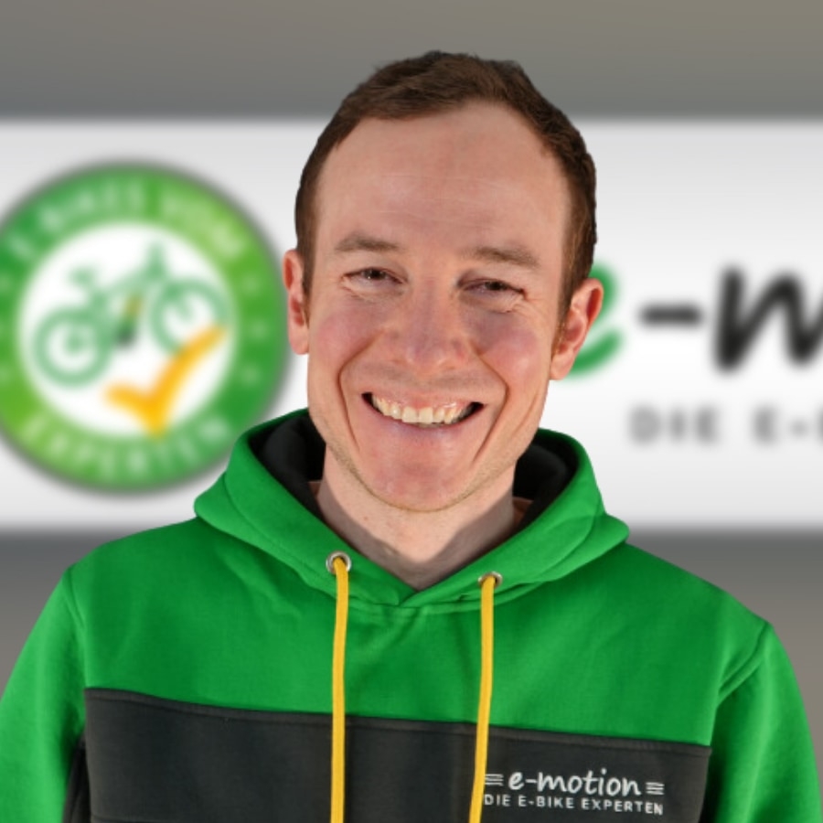 Ein Mitarbeiter von E-Motion mit grünem Hoodie vor dem Logo. Entdecken Sie die Welt der E-Bikes mit unseren Experte