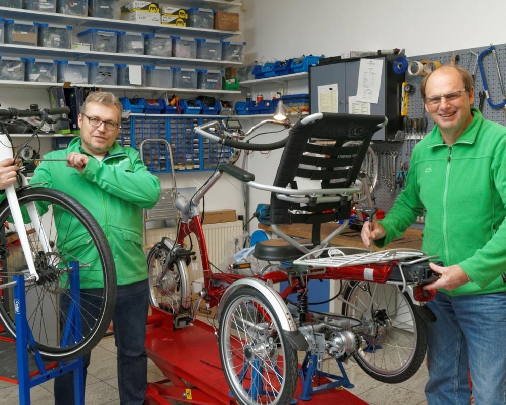 Zwei Techniker warten ein komplexes E-Bike in einer gut ausgestatteten Werkstatt. Ideal für professionelle E-Bike P