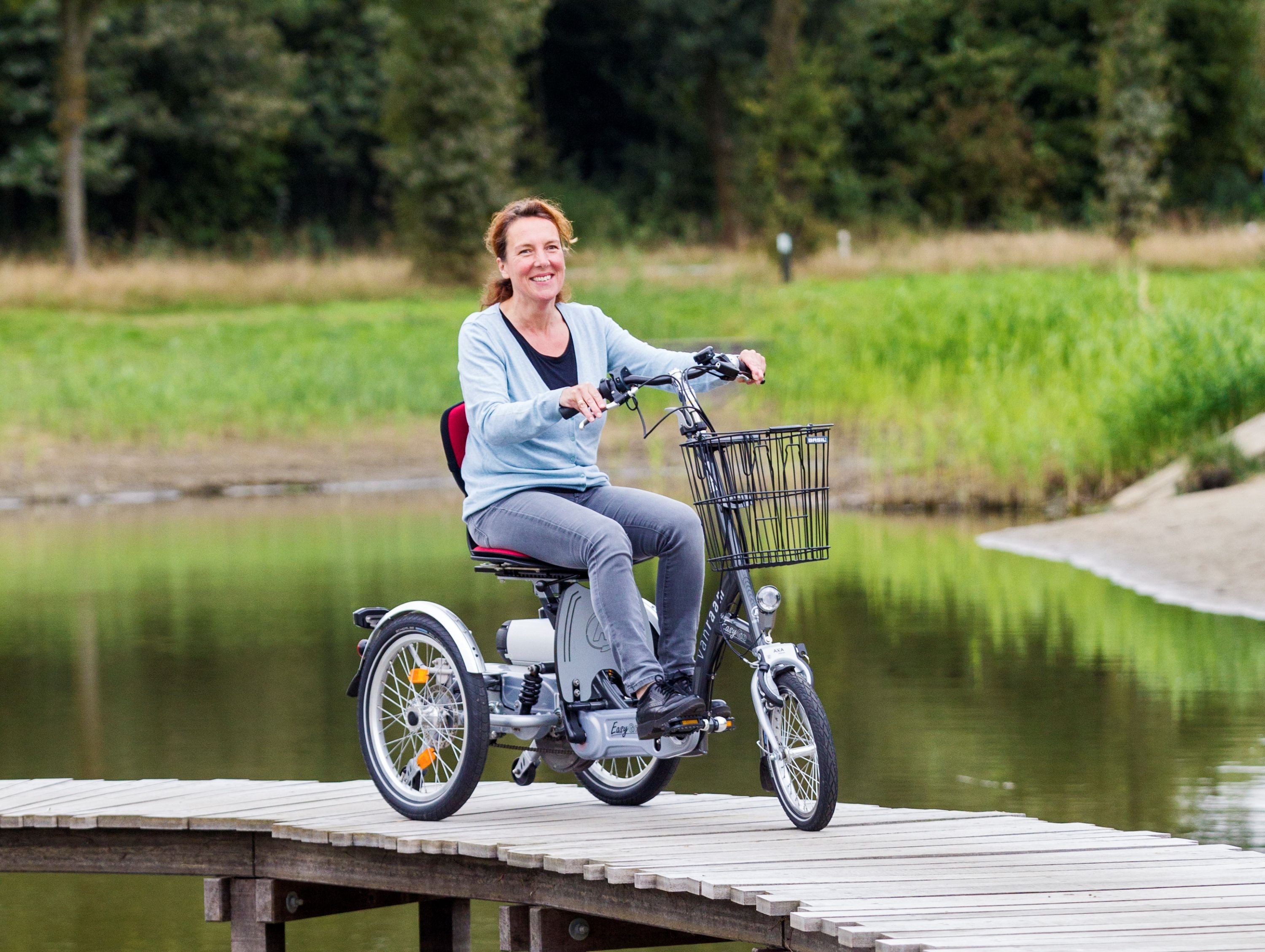 Frau fährt mit einem Dreirad von Van Raam über eine Holzbrücke über einem Teich.
