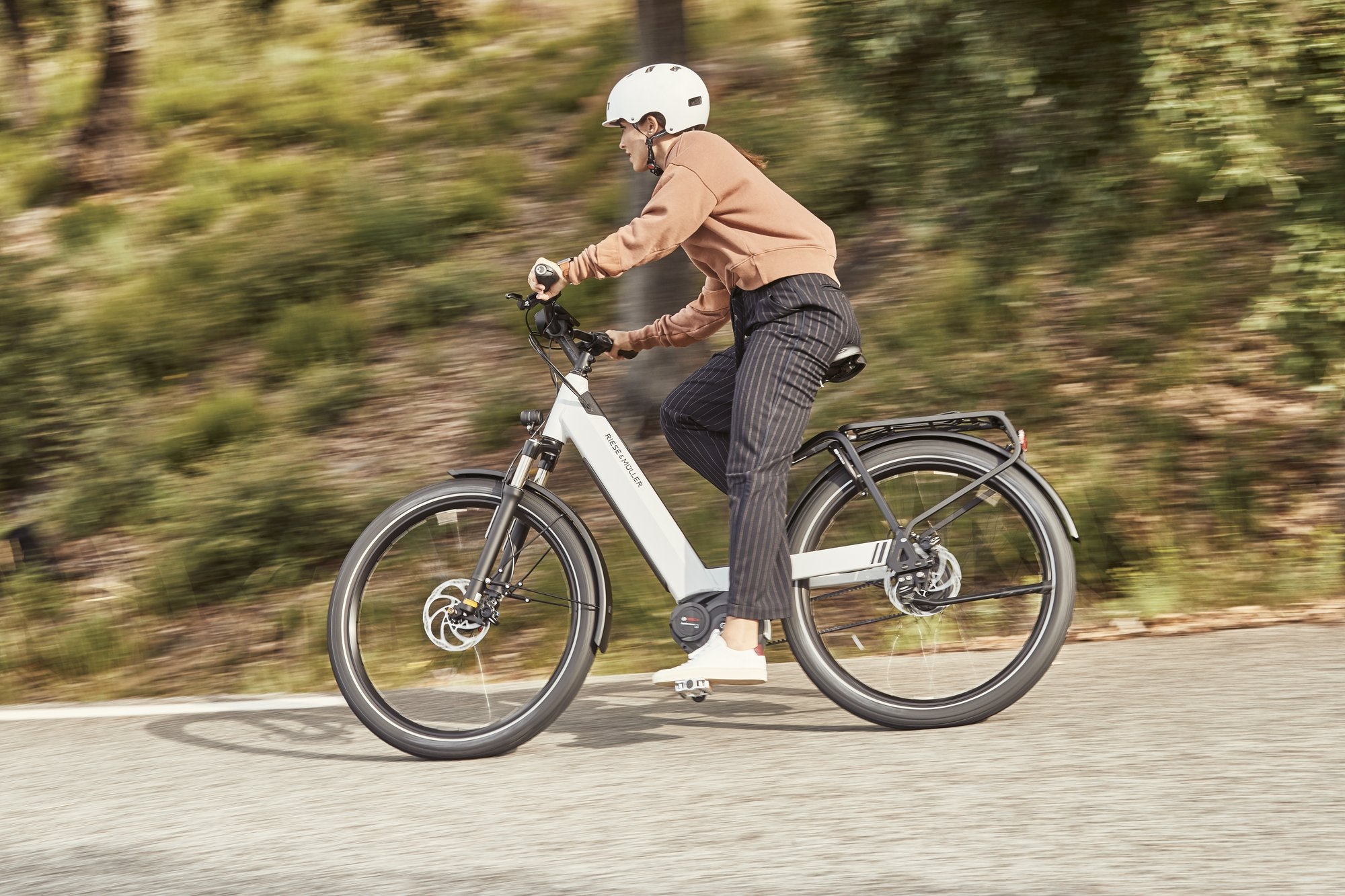 Eine Person fährt ein modernes E-Bike auf einer asphaltierten Straße, umgeben von grüner Landschaft. Das E-Bike hat