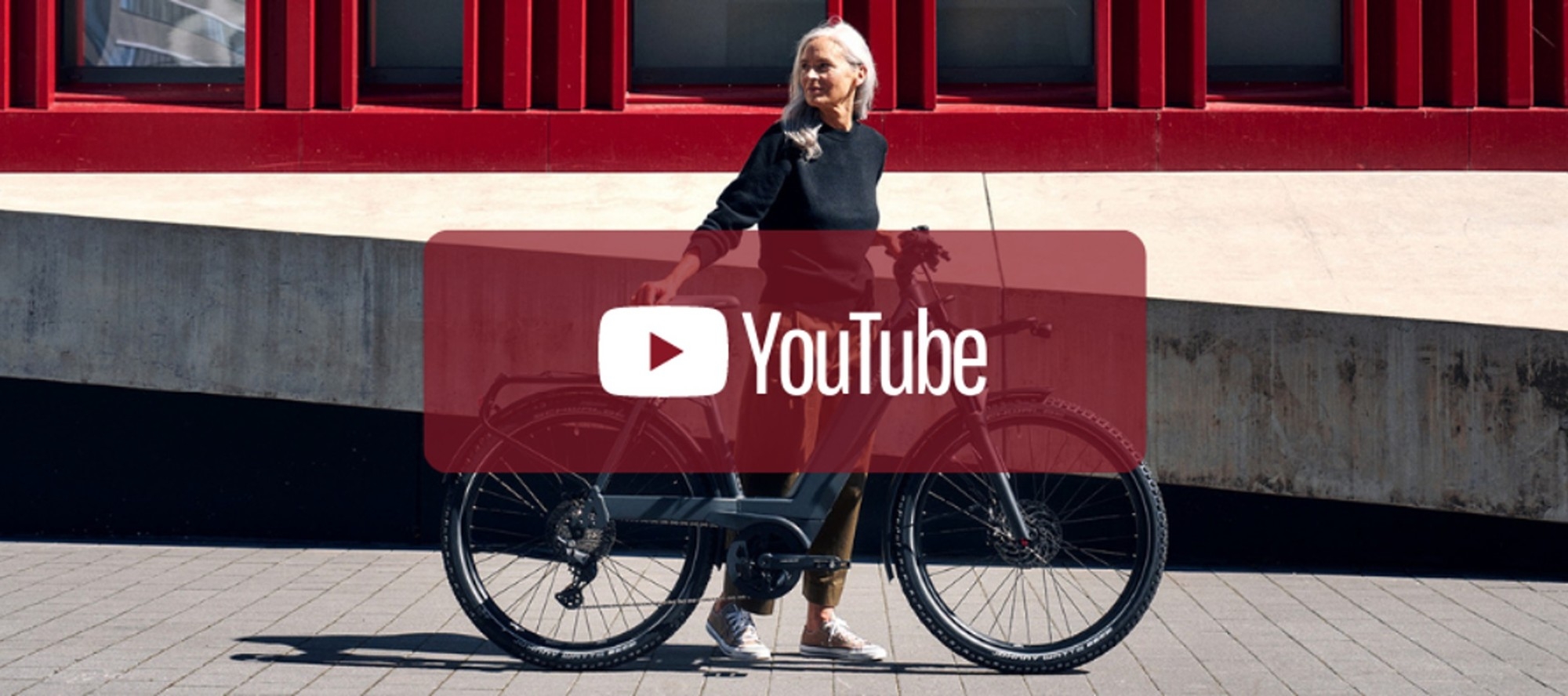 Das Bild zeigt eine Frau, die neben einem Riese & Müller E-Bike steht und in einer urbanen Umgebung posiert.