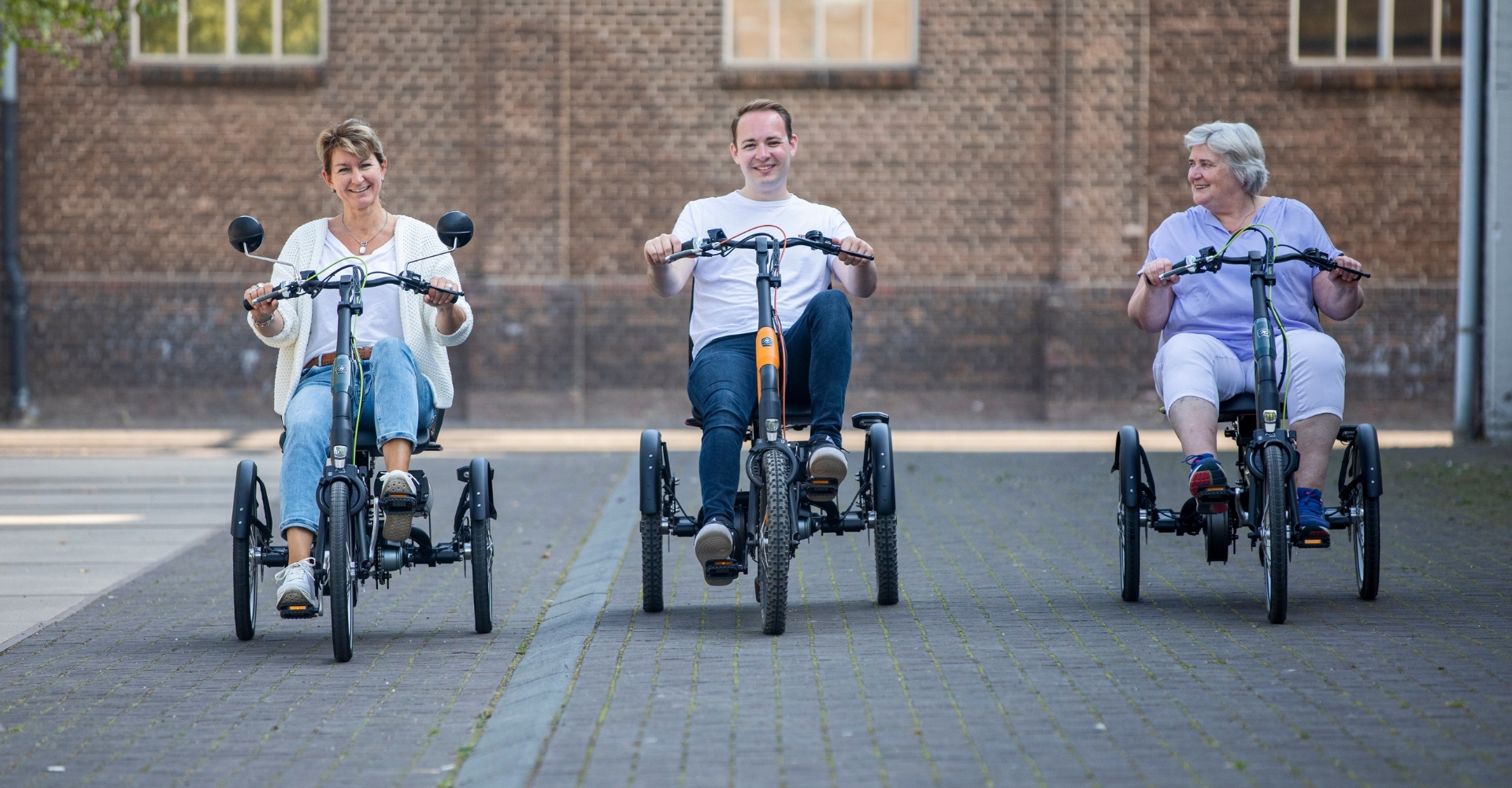 Drei Leute sind auf Van Raam Dreirädern unterwegs beim Probefahren auf der REHAB Messe in Karlsruhe.