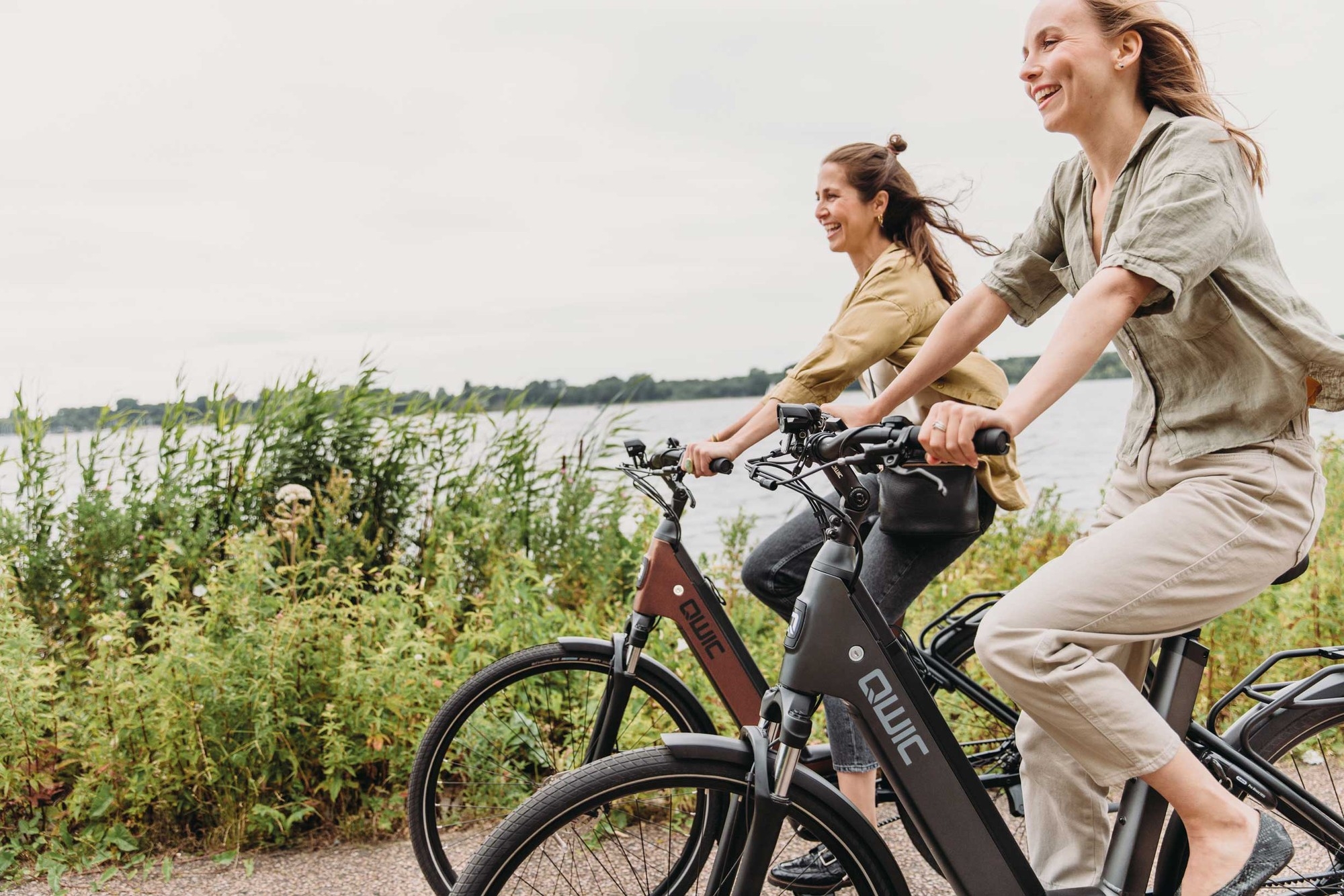 Das Bild zeigt zwei Frauen, die auf QWIC Mira Tour E-Bikes fahren.