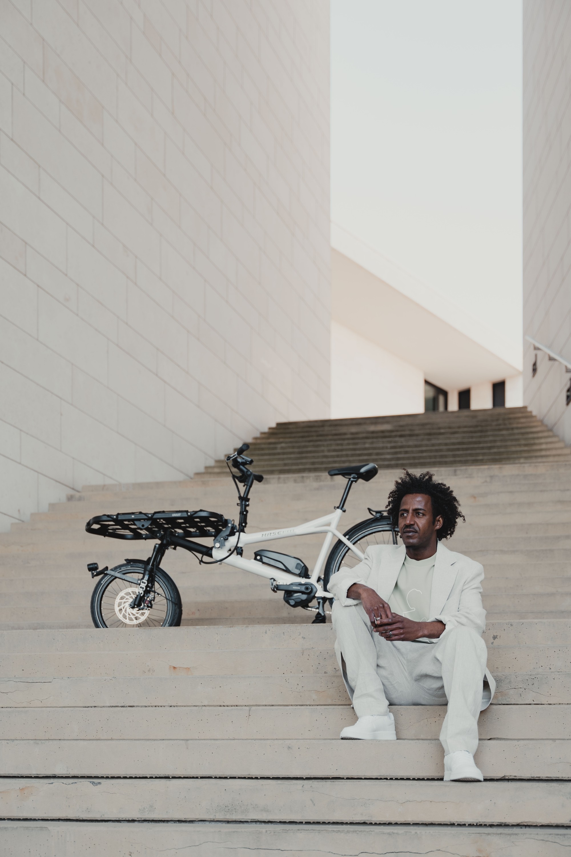 Ein Junger Mann sitzt mit seinem Hase City e-Bike auf einer Treppe in Berlin Mitte.