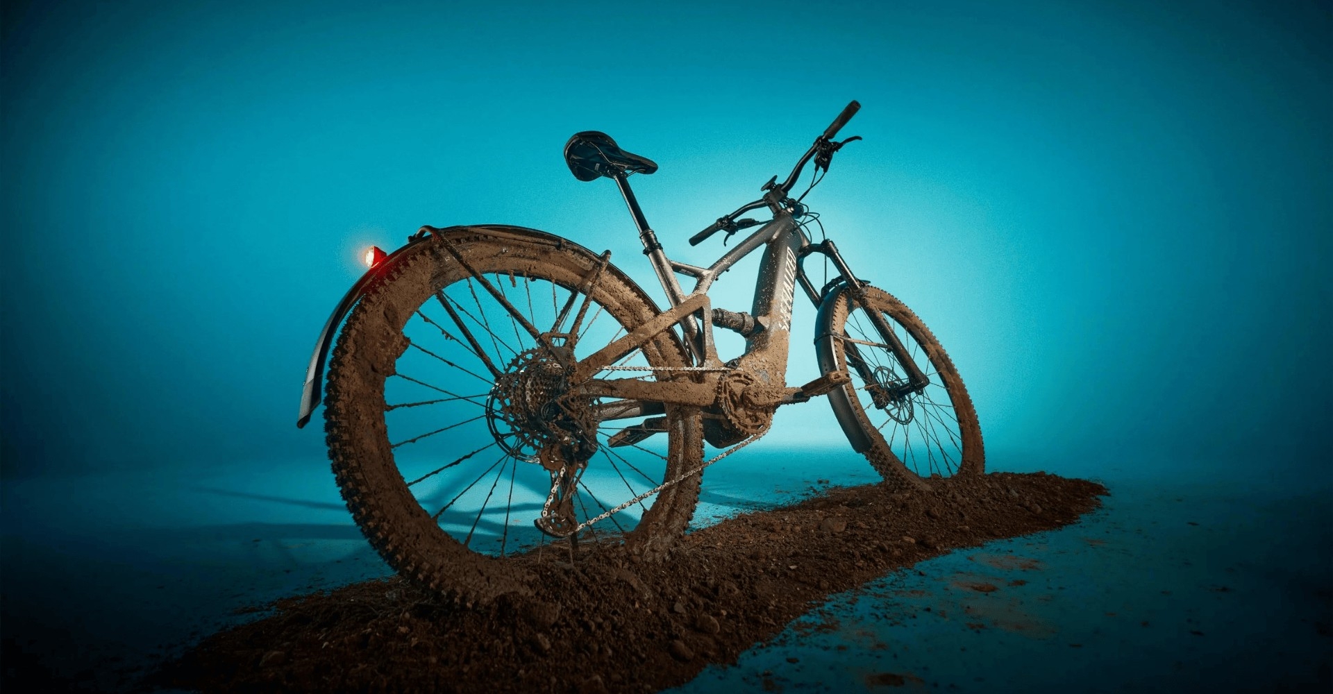 Das Specialized Turbo Tero X vor blauem Hintergrund auf einer Spur aus Erde stehend