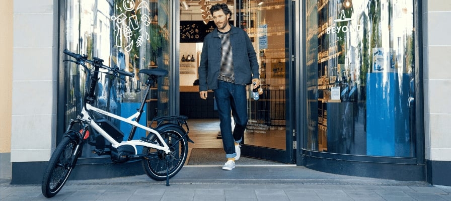Ein Mann verlässt ein Geschäft. Vor dem Eingang steht ein Riese & Müller Tinker Vario 2022 e-Bike.