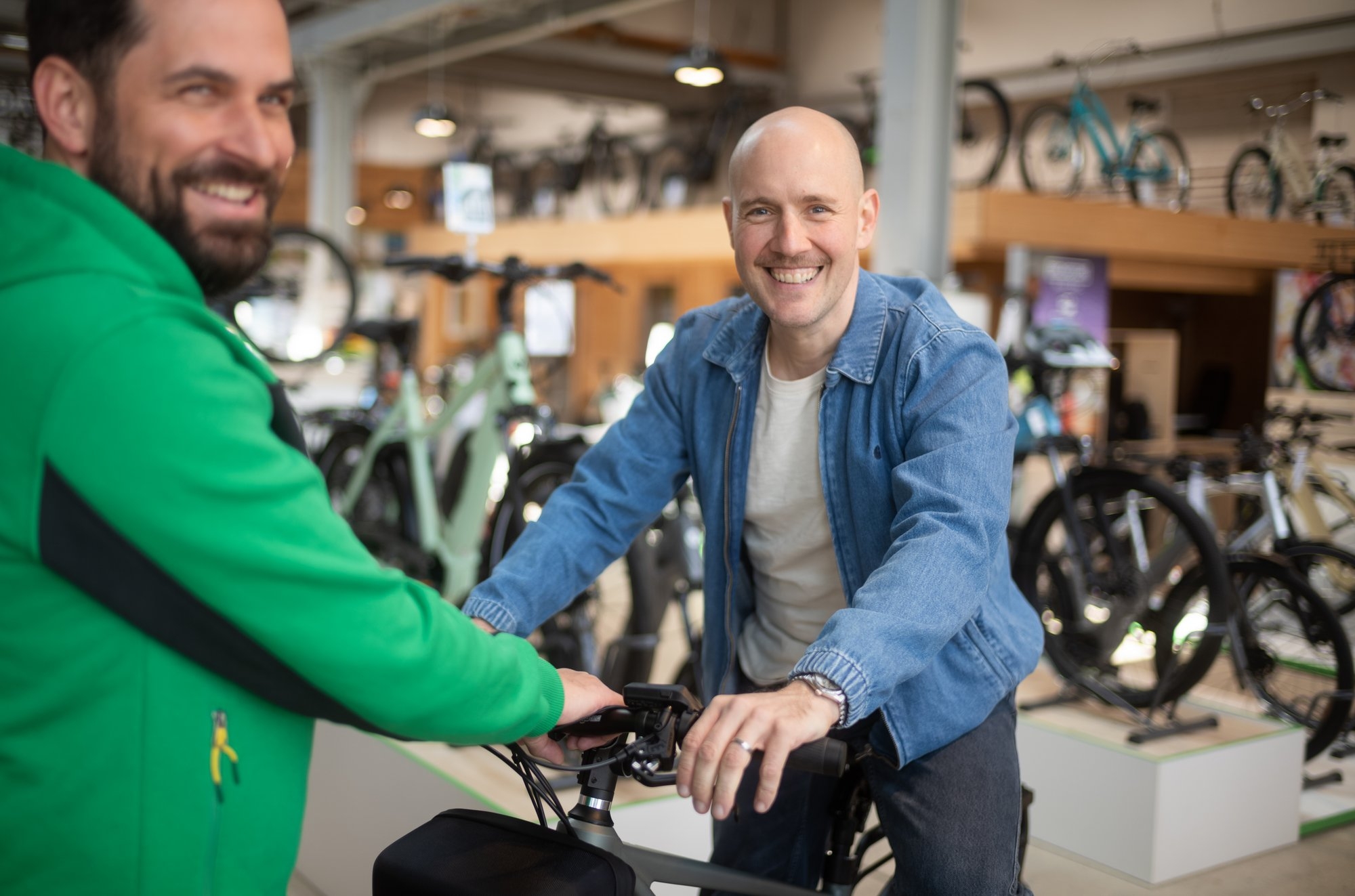 Zwei Männer stehen in einem Fahrradgeschäft. Der Mann in der blauen Jacke sitzt auf einem e-Bike und lächelt in die