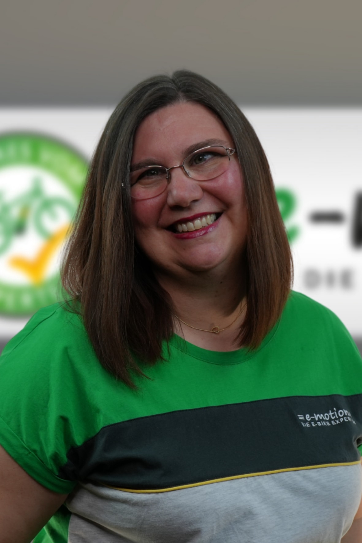 Freundliche e-motion Mitarbeiterin im grünen Shirt vor einem Firmenlogo. Perfekte Wahl für professionellen Service