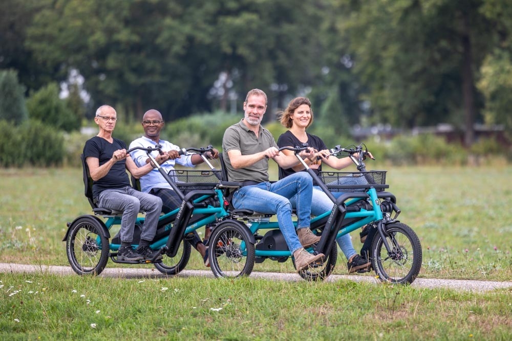 Das Bild zeigt zwei Van Raam Fun2Go E-Bikes, die in einer ländlichen Umgebung auf einem Weg platziert sind.
