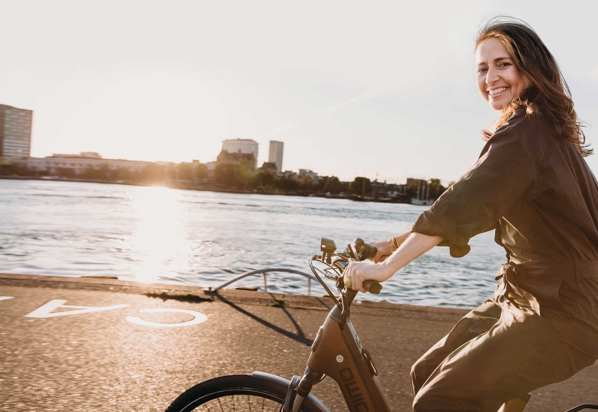 Eine Frau fährt auf dem QWIC Mira e-Bike am Wasser entlang