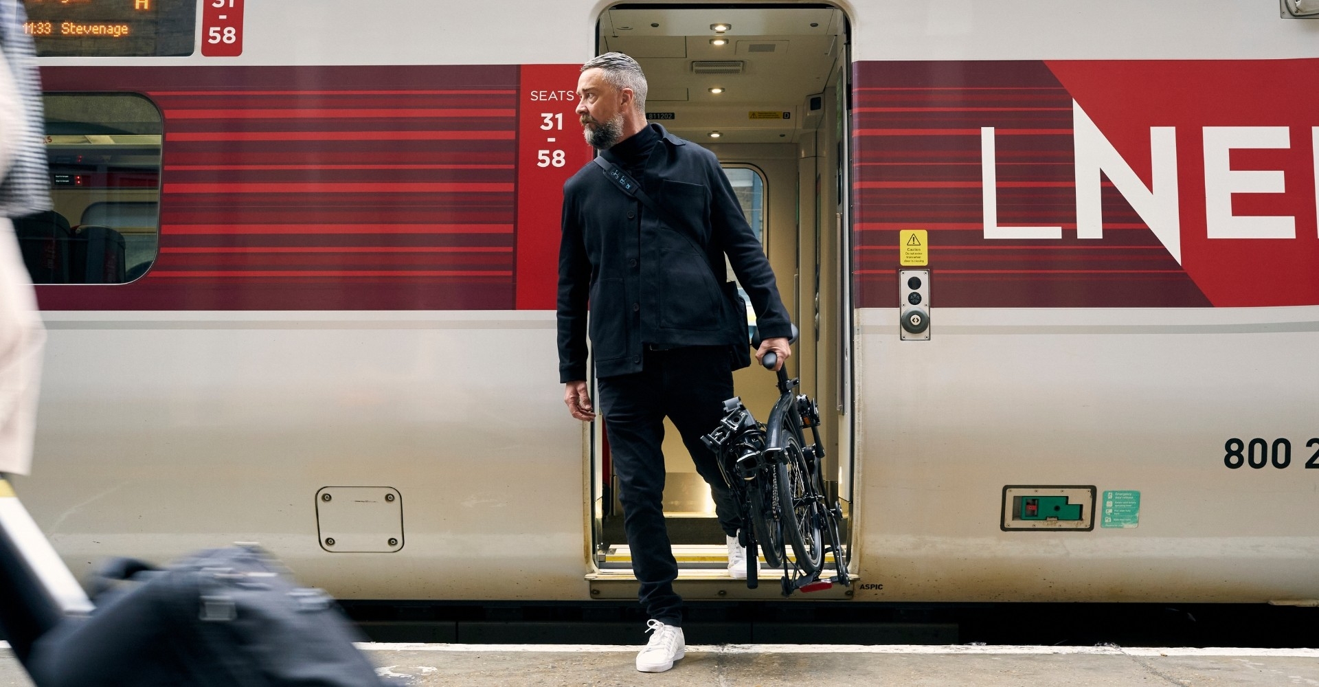 Mann steigt aus Zug mit dem Kompakt e-Bike P Line Brompton