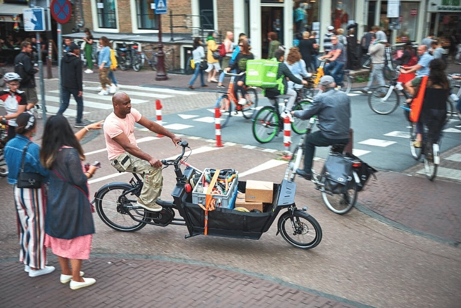 Mann fährt Lastenrad mit Paketen in belebter Stadtstraße